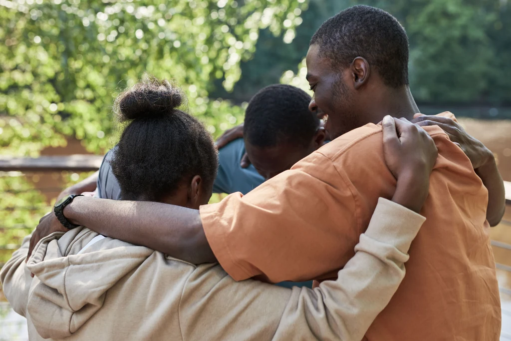 Three people embracing and supporting one another outdoors