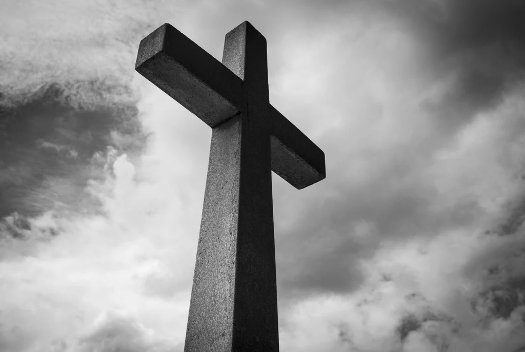 A stone cross against a cloudy sky, photographed in black and white